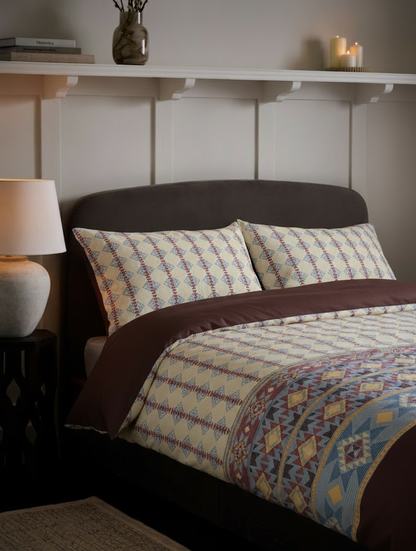 Bedroom with a bed featuring a patterned comforter, pillows, and a nightstand with a lamp.