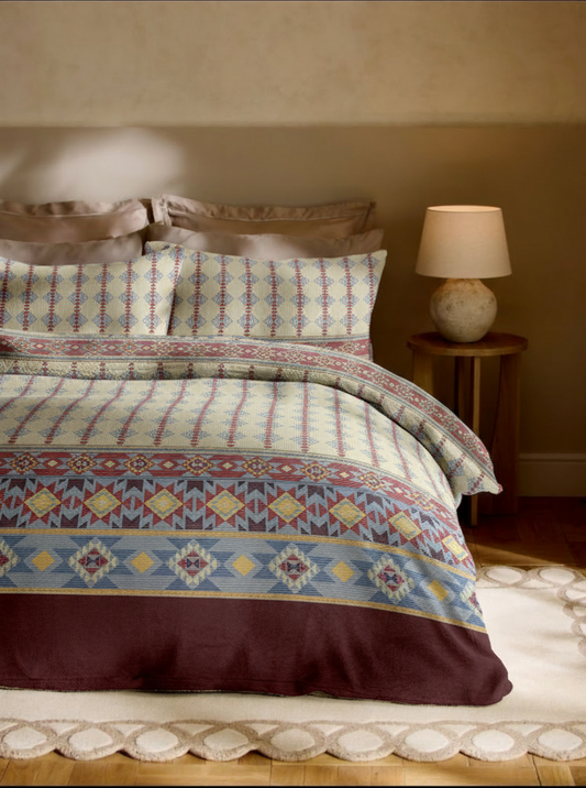 Bed with patterned bedding and a lamp on a nightstand in a bedroom setting.