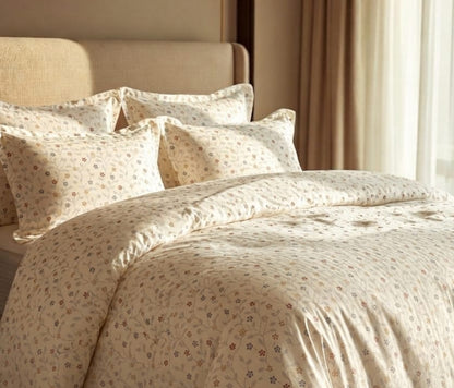 A neatly made bed with a cream-colored duvet cover and matching pillowcases featuring a delicate, small-scale floral pattern in muted red, blue, and green tones. The bed is styled in a warm, softly lit bedroom with a beige upholstered headboard and neutral curtains.