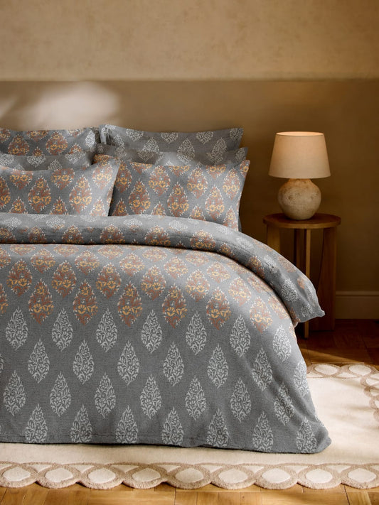 Patterned gray bedding set on a bed with a lamp in the background