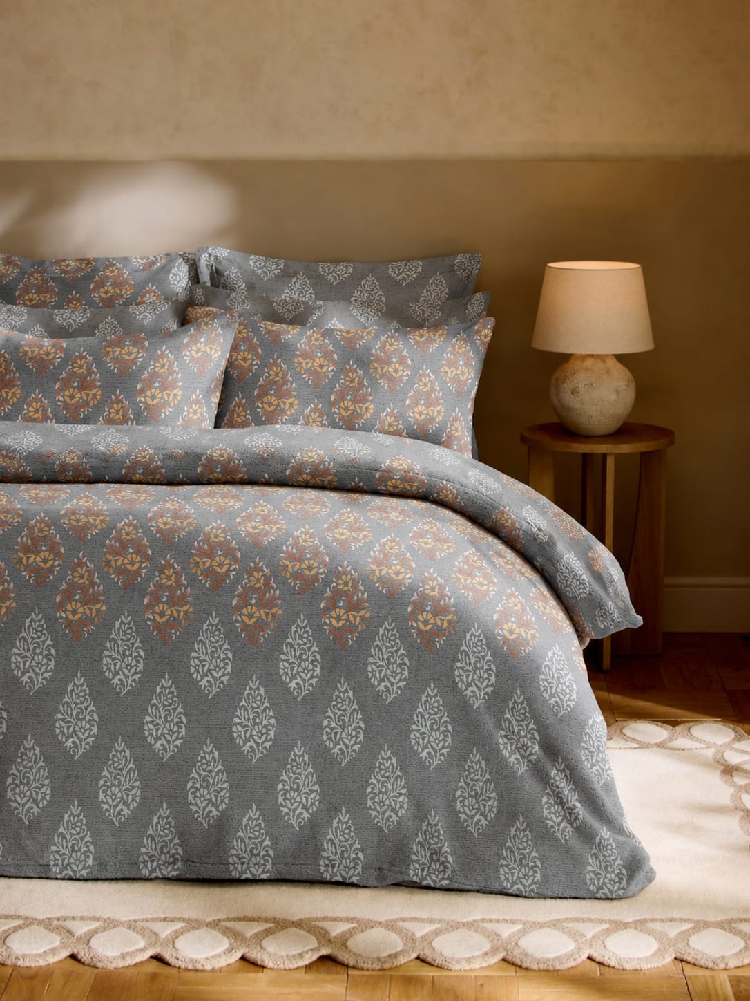 Patterned gray bedding set on a bed with a lamp in the background