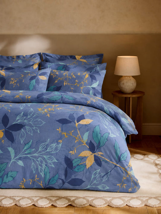 Blue floral bedding set on a bed with a lamp on a nightstand in the background.