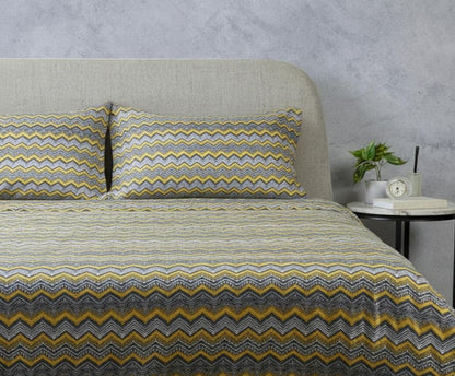 Bed with zigzag patterned bedding and pillows against a gray wall.