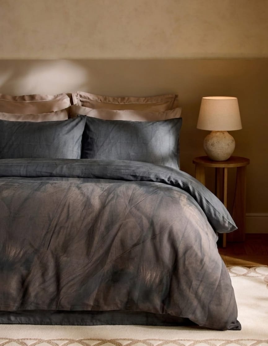 Gray bedding set on a bed with a lamp on a side table in a bedroom.