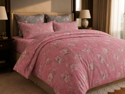 A bed dressed in a pink floral duvet cover and matching pillow shams, styled in a warm bedroom setting with bedside tables, lamps, and curtains.
