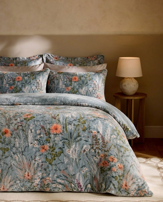 Floral patterned bedding set on a bed with a lamp on a side table in the background.